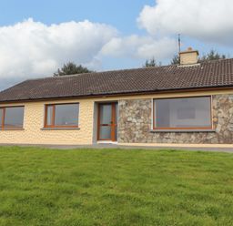 A single-story house with three large windows and a door on a grassy lawn at Gortnamona in Coolnaharragill Lower near Glenbeigh County Kerry