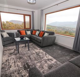 A living room with grey sofas orange and patterned cushions a small table and large windows showing a mountain view at Gortnamona in Coolnaharragill Lower near Glenbeigh County Kerry