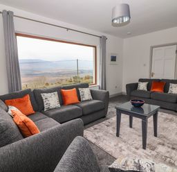A living room with two grey sofas and orange cushions a glass coffee table and large window showing a landscape view at Gortnamona in Coolnaharragill Lower near Glenbeigh County Kerry