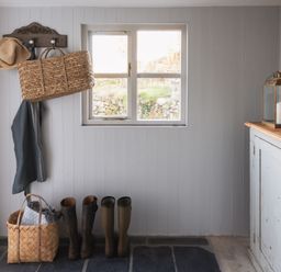 An entryway with a window a wooden coat rack with hats and bags rubber boots on the floor a basket with blankets and a cabinet with a lantern and candle at Butterwell Cottage at Collihole in Chagford
