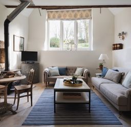 A living room with two sofas a coffee table a blue striped rug a small dining table with wooden chairs and a fireplace at Butterwell Cottage at Collihole in Chagford
