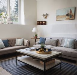 A sitting area with two sofas a coffee table with books and a tray with fruit and a glass a side table with a lamp and a plant and a wall painting at Butterwell Cottage at Collihole in Chagford
