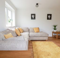 A living room with a grey sofa with yellow cushions a yellow rug wooden coffee table with a lamp and plants at Chynoweth House in Cubert