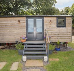 An outdoor wooden cabin with black double doors stone stairs and flower pots at Shepherds Stone in Llanfairynghornwy near Llanfaethlu