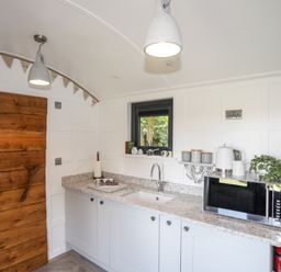A kitchen with white cabinets granite countertop microwave kettle and wooden door at Shepherd's Stone in Llanfairynghornwy near Llanfaethlu