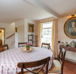 A dining room with a round table covered by a patterned tablecloth and wooden chairs at Chalkpit Cottage in Blewbury