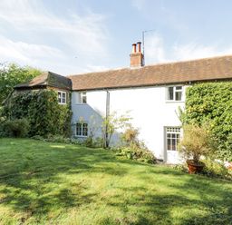 A white house with a tiled roof surrounded by grass and plants at Chalkpit Cottage in Blewbury