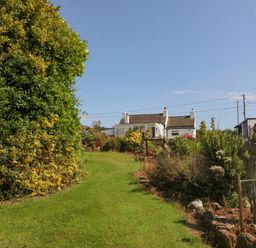 A garden with a grass path leading to a white house with a conservatory and statues in the garden at Pen Bonc in Llanddaniel Near Gaerwen