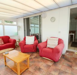 A conservatory with red sofas and a coffee table at Pen Bonc in Llanddaniel Near Gaerwen
