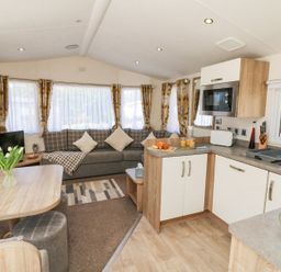 An open plan living area with a kitchen and dining table with flowers and a living room with a sofa and TV at Horizon in Combe Martin