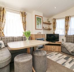 A living room with two grey sofas a wooden table and two stools a television on a wooden stand and curtains at Horizon in Combe Martin