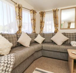 A corner sofa with cushions and a rolled towel in a living room with floral curtains and a wall mirror at Horizon in Combe Martin