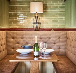 A dining nook with a wooden table set with plates glasses a bottle and a pot at The Stallion in Humshaugh