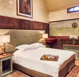 A bedroom with a double bed a tray with coffee and croissants two bedside tables with lamps a chest of drawers with flowers and a framed horse picture on the wall at The Stallion in Humshaugh