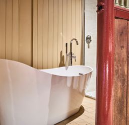 A bathroom with a white freestanding bathtub and a red wooden partition at The Stallion in Humshaugh