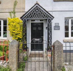 The front entrance of a cottage with a black wooden door and a black metal porch covering at Hobbs Cottage in Sticklepath