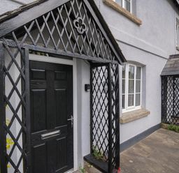 A black door with a lattice porch and window on the side of a light grey building at Hobbs Cottage in Sticklepath