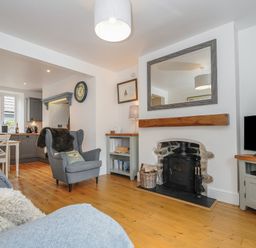 A living room with a fireplace armchair and television next to an open kitchen at Hobbs Cottage in Sticklepath
