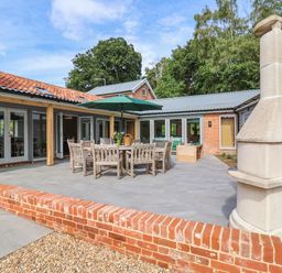 A patio area with wooden dining table and chairs under a green umbrella next to a chimney at Church Farm Barn Dunwich near Westleton