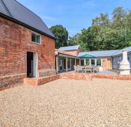 An outdoor patio area with brick buildings gravel ground and wooden table with chairs and umbrella at Church Farm Barn Dunwich near Westleton
