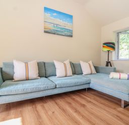 A living room with a light blue sectional sofa with cushions a colorful floor lamp and a painting on the wall at Church Farm Barn in Dunwich near Westleton