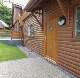 An exterior view of a brown wooden lodge with a door numbered 16 and windows surrounded by grass at Classic Lodge 16 in Dyserth