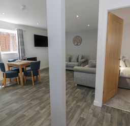 A dining area with table and chairs next to a living area with sofas and an open door leading to a bedroom at Classic Lodge 16 in Dyserth