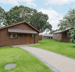 A pathway leading to wooden lodges surrounded by grass and trees at Luxury Lodge 69 in Dyserth