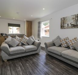 A living room with two grey sofas with cushions and a kitchen area with wooden cabinets at Luxury Lodge 69 in Dyserth