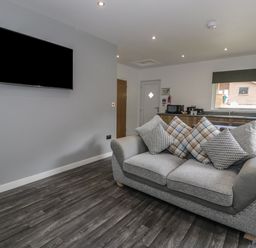 A living room with a sofa and cushions a wall mounted tv and a kitchen area at Luxury Lodge 69 in Dyserth