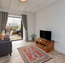 A living room with a gray sofa orange and patterned cushions a wooden TV stand with a television a patterned rug and open doors to a patio at Rowan Barn in Bellingham