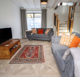 A living room with two grey sofas with orange and patterned cushions a wooden tv stand and a red patterned rug at Rowan Barn in Bellingham