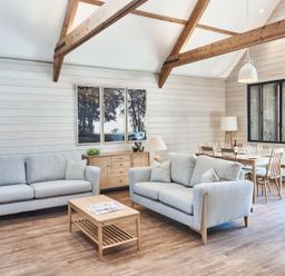A living room with two sofas a coffee table and a dining table under wooden beams at The Hayloft in Humshaugh