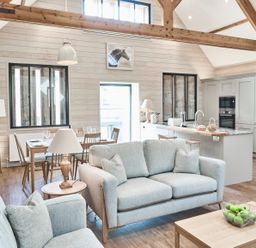 An open plan living room and kitchen with sofas, dining table, kitchen island, and wooden beams at The Hayloft in Humshaugh