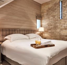 A bedroom with a bed with white linens two bedside tables with lamps and a tray with beverages and newspapers at The Hayloft in Humshaugh