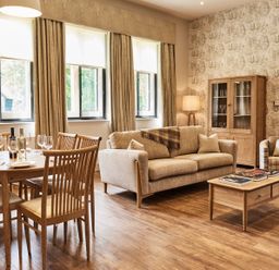 A living room with a dining table set with wine and plates and a sofa and armchair at The Stalls in Humshaugh