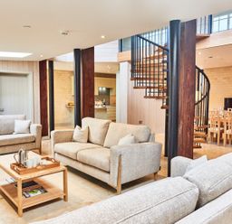 A living room with beige sofas a wooden coffee table a spiral staircase and a dining table at The Carriage House in Humshaugh