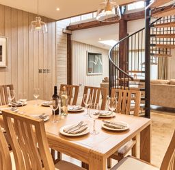 A dining area with a wooden table set with plates wine glasses and bottles near a spiral staircase and a living room at The Carriage House in Humshaugh