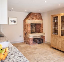 A kitchen with a brick fireplace a wooden cabinet with glass doors and a countertop with a fruit basket at The Smithy in Humshaugh