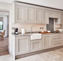 A kitchen with light-colored cabinets a granite countertop and a dining table visible in the background at The Smithy in Humshaugh