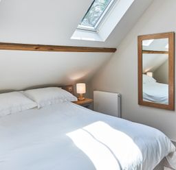 A bedroom with a bed a nightstand with a lamp a mirror and a skylight window at The Smithy in Humshaugh