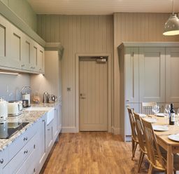 A kitchen with wooden floor gray cabinets a dining table set with plates wine glasses and a bottle at The Foal in Humshaugh