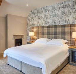 A bedroom with a bed with white bedding two bedside tables with lamps and a patterned wall at The Foal in Humshaugh