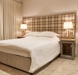 A bedroom with a bed with white bedding a plaid headboard two bedside tables with lamps and beige curtains at The Foal in Humshaugh