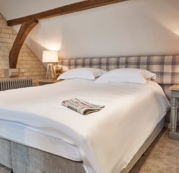 A bedroom with a bed covered in white linens and a newspaper on top two bedside tables with lamps and a wooden beam on the wall at The Foal in Humshaugh