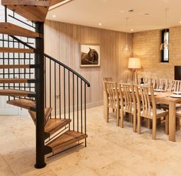A dining room with a wooden table and chairs next to a spiral staircase at The Clocktower in Humshaugh