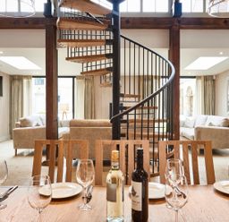 A dining table set with glasses plates and wine bottles in a room with spiral staircase and sofas at The Clocktower in Humshaugh