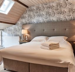 A bedroom with a bed with folded towels a skylight window and bedside lamps at The Clocktower in Humshaugh