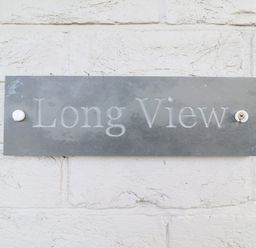 A metal sign with the words Long View mounted on a white brick wall at Long View in Southwold