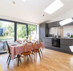A kitchen with gray cabinets a dining table set with dishes and glasses and sliding glass doors leading to a garden at Long View in Southwold